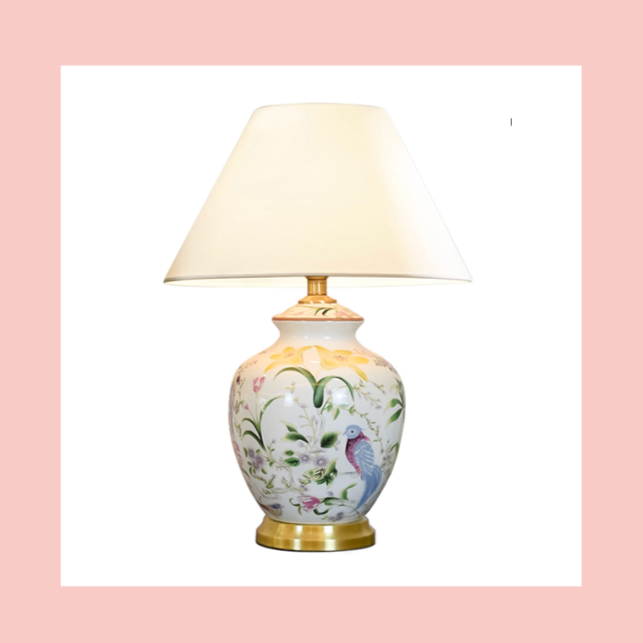 Decorative porcelain table lamp with a floral and bird design, cream-colored lampshade, and gold accents.