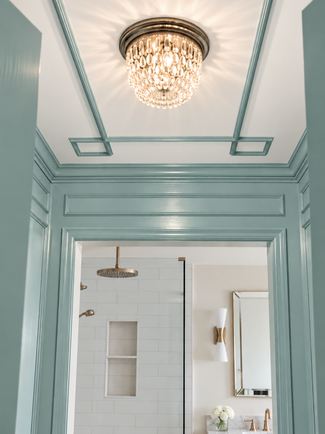 Elegant bathroom viewed through an open doorway with a decorative ceiling and chandelier, gold fixtures, and a large mirror.