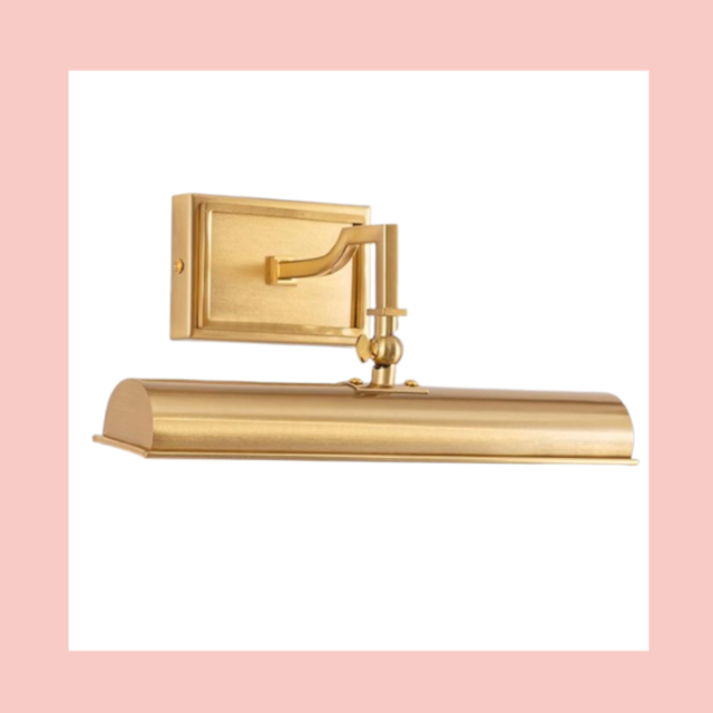 A gold picture light fixture with a painted arm and mounting plate, designed to illuminate a framed artwork.