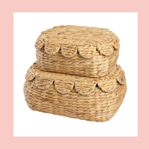 Two stacked woven wicker containers with lids, set against a pink background.