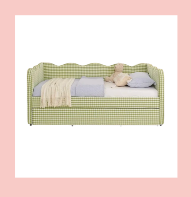 A green gingham daybed with a backrest, decorated with a beige blanket, a blue pillow, and a bunch of stuffed animals, set against a pink background with a white border.
