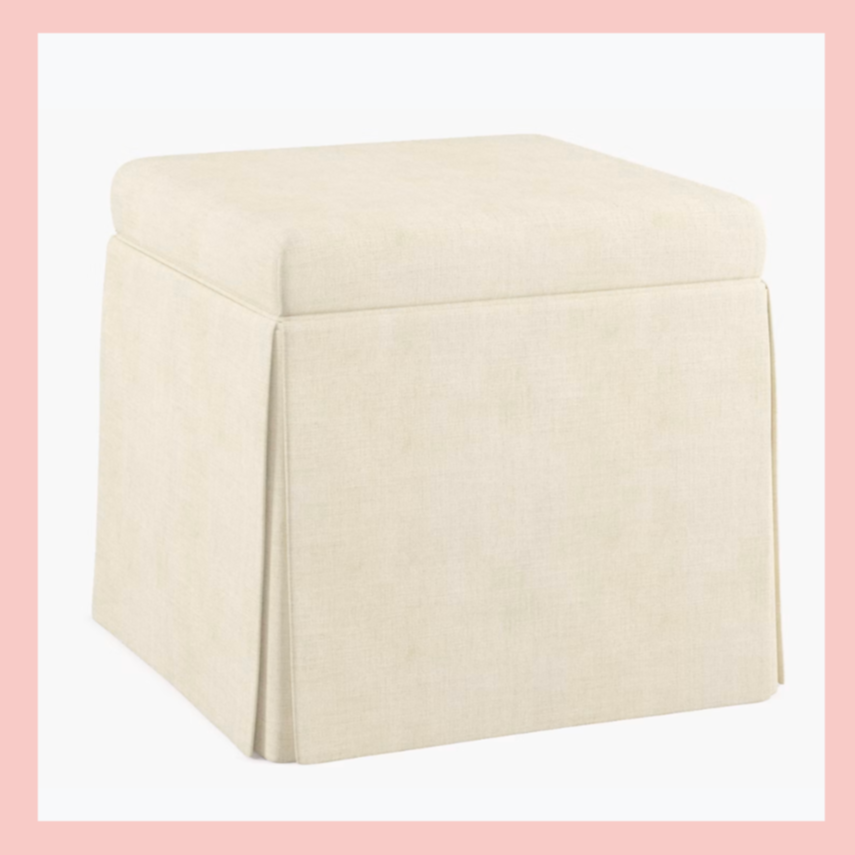 Cream-colored upholstered ottoman with a boxy shape and sloped sides.