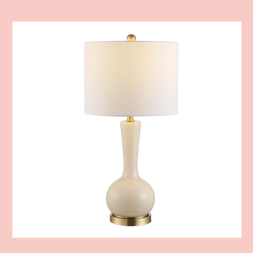 A white table lamp with a rounded base and a beige lampshade, set against a light pink background.