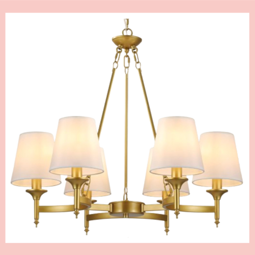 A gold chandelier with eight white lampshades against a pink background.