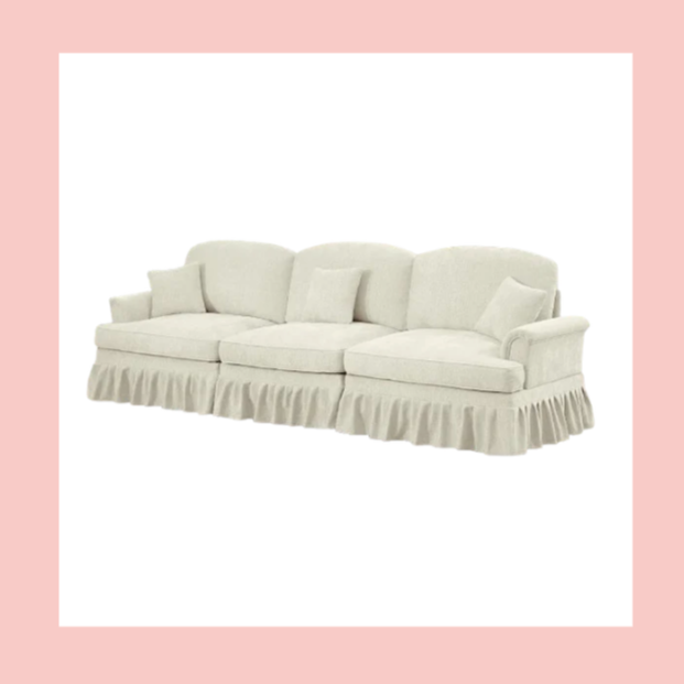 A white upholstered sofa with three seat cushions, three back cushions, and a pleated skirt around the base, against a white background with a pink border.