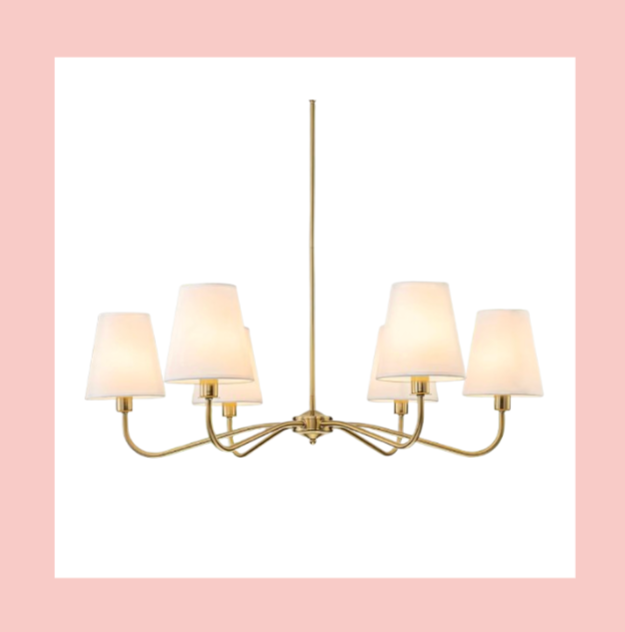 A modern chandelier with six white lampshades and a gold finish hanging from a ceiling.