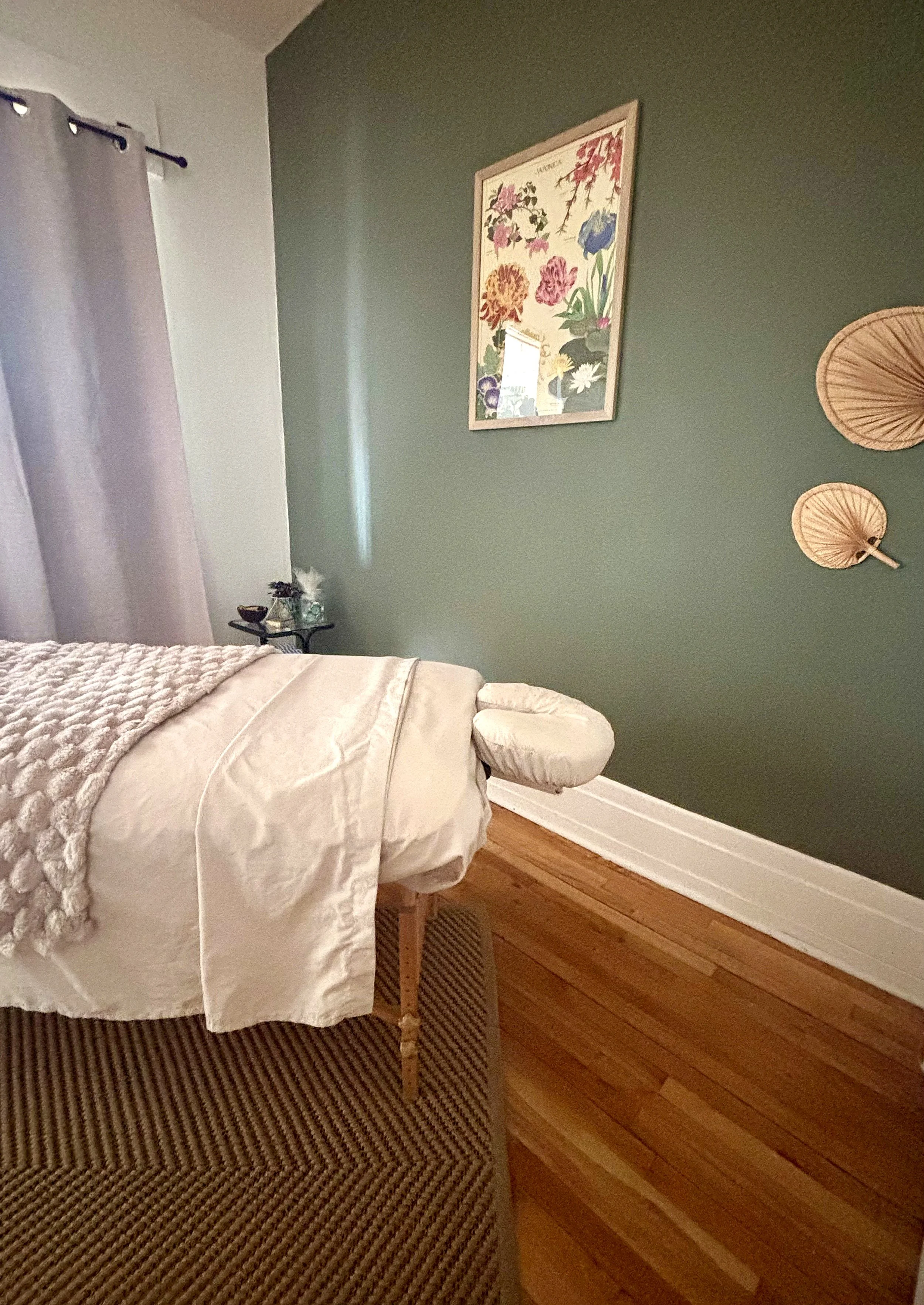 Chambre avec un lit blanc, une tête de lit rembourrée, un tapis rayé, un mur vert foncé avec des décorations murales en forme d’éventail en bois et un tableau floral.