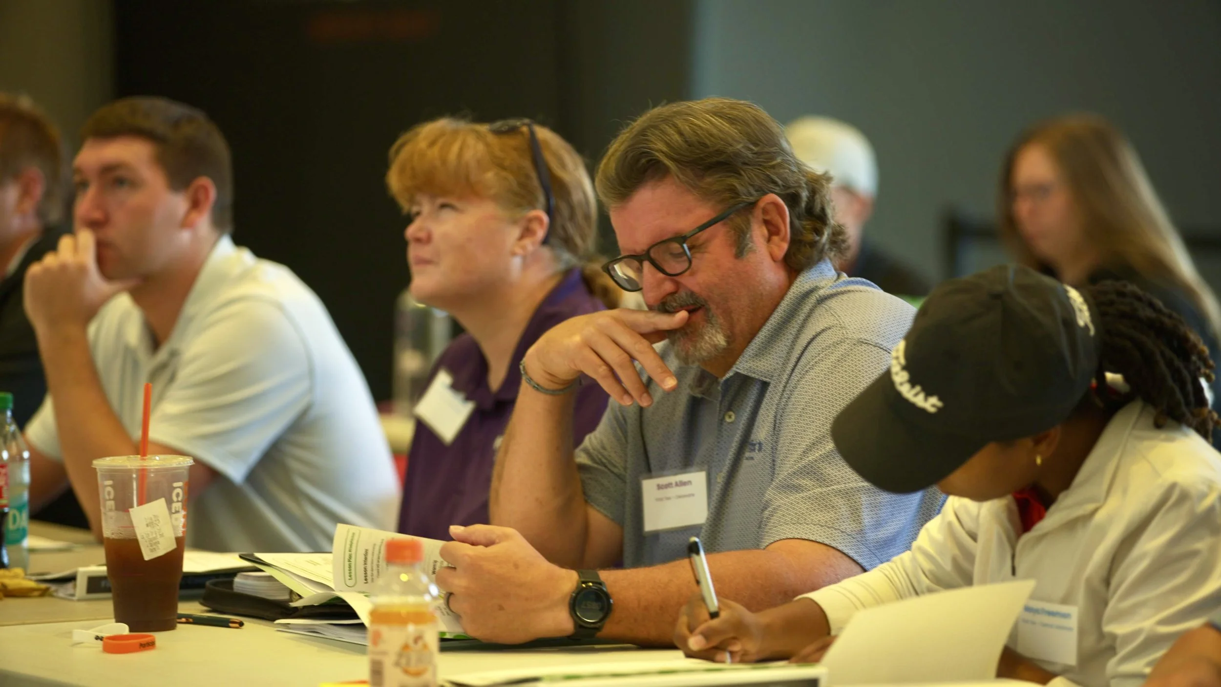 People sitting at a conference table, reading and listening during a meeting or seminar.