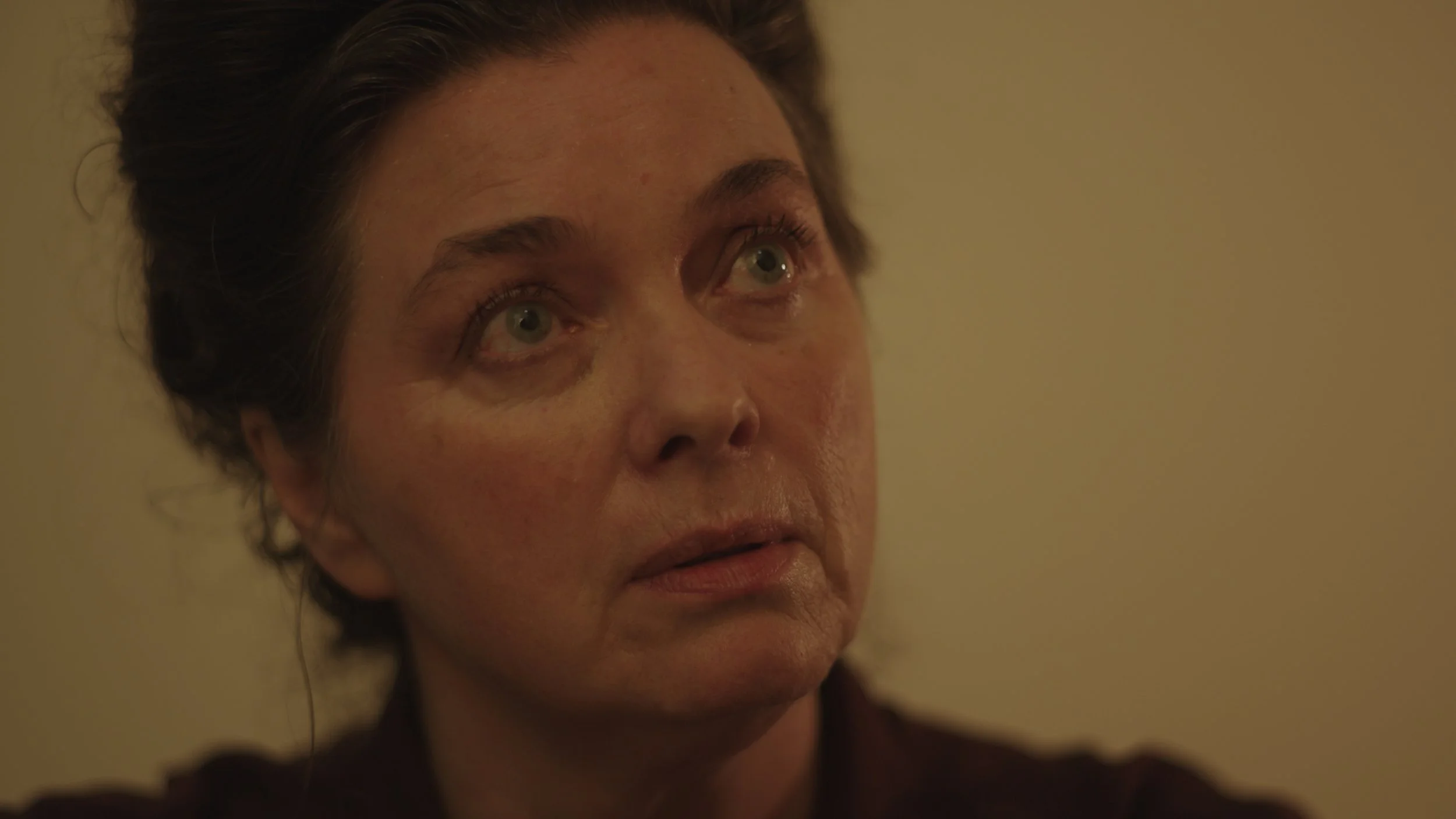 Close-up of a middle-aged woman with short dark hair, looking upward with a serious expression against a plain background.