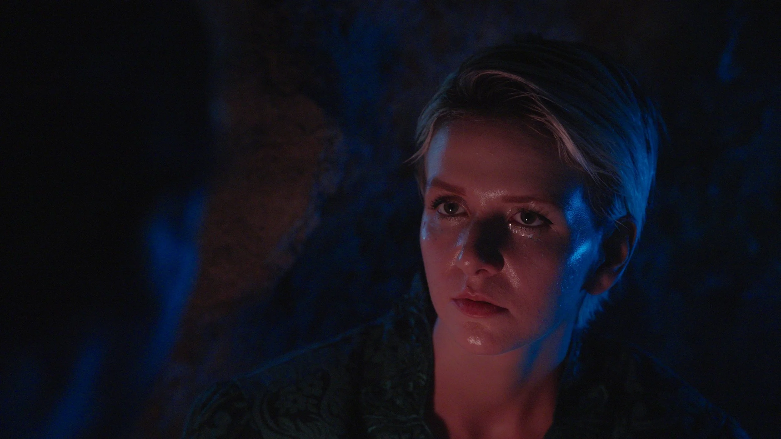 Close-up of a woman with short, styled hair and makeup, with dramatic lighting and a dark background.