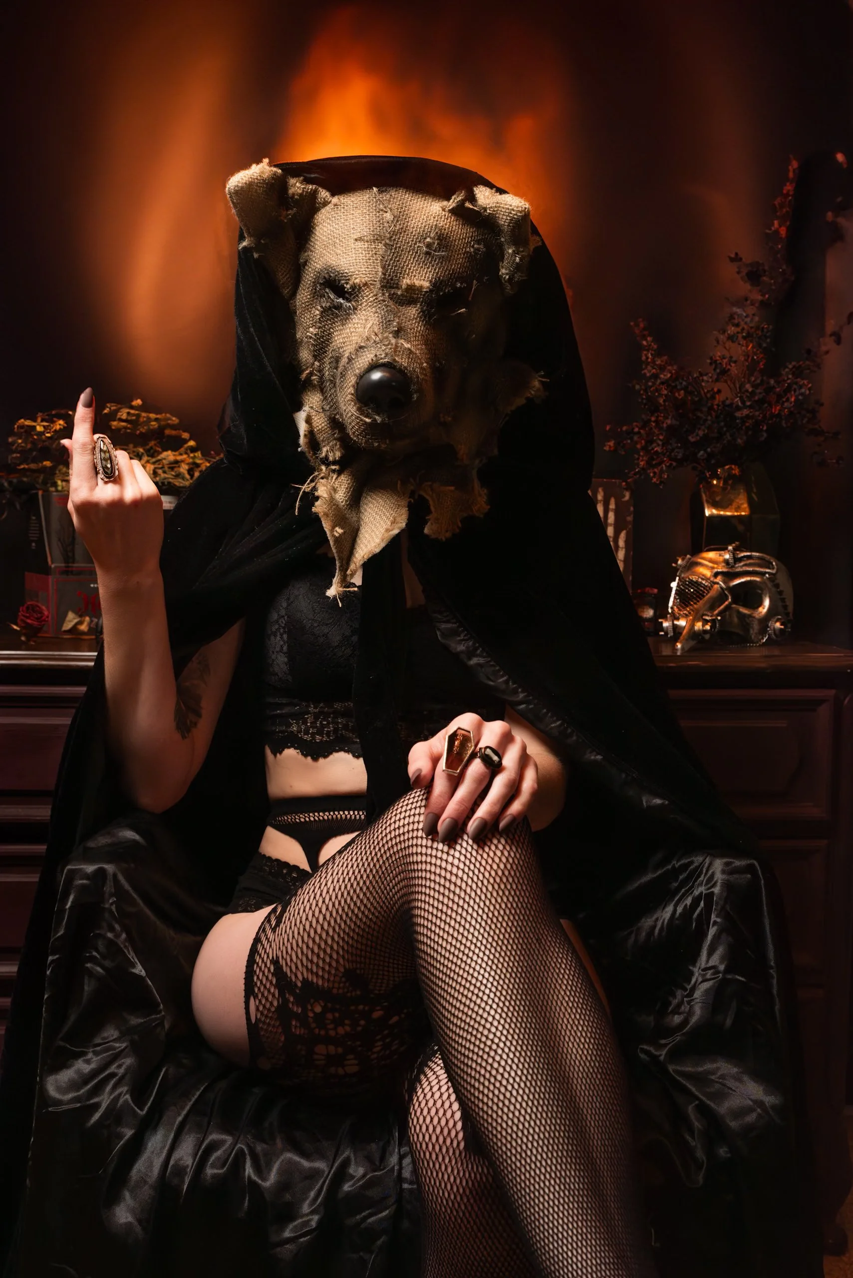 A person wearing a bear mask, black cape, fishnet stockings, and lingerie, sitting on a fireplace mantle in a dimly lit room with orange lighting and dark decor.