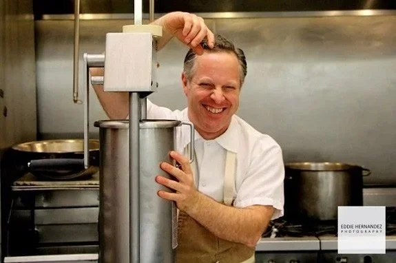 Chef smiling in a commercial kitchen, operating a large piece of cooking equipment.
