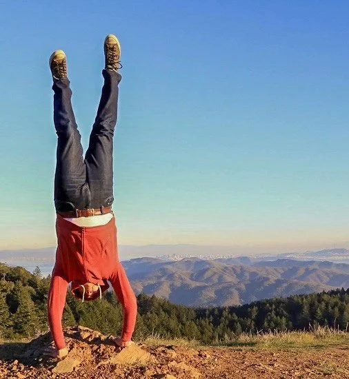 Person doing a handstand on a hilltop with mountains in the background on a clear day.