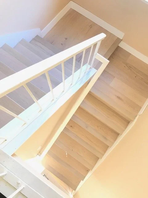 Top view of a wooden staircase with white railing and beige walls.