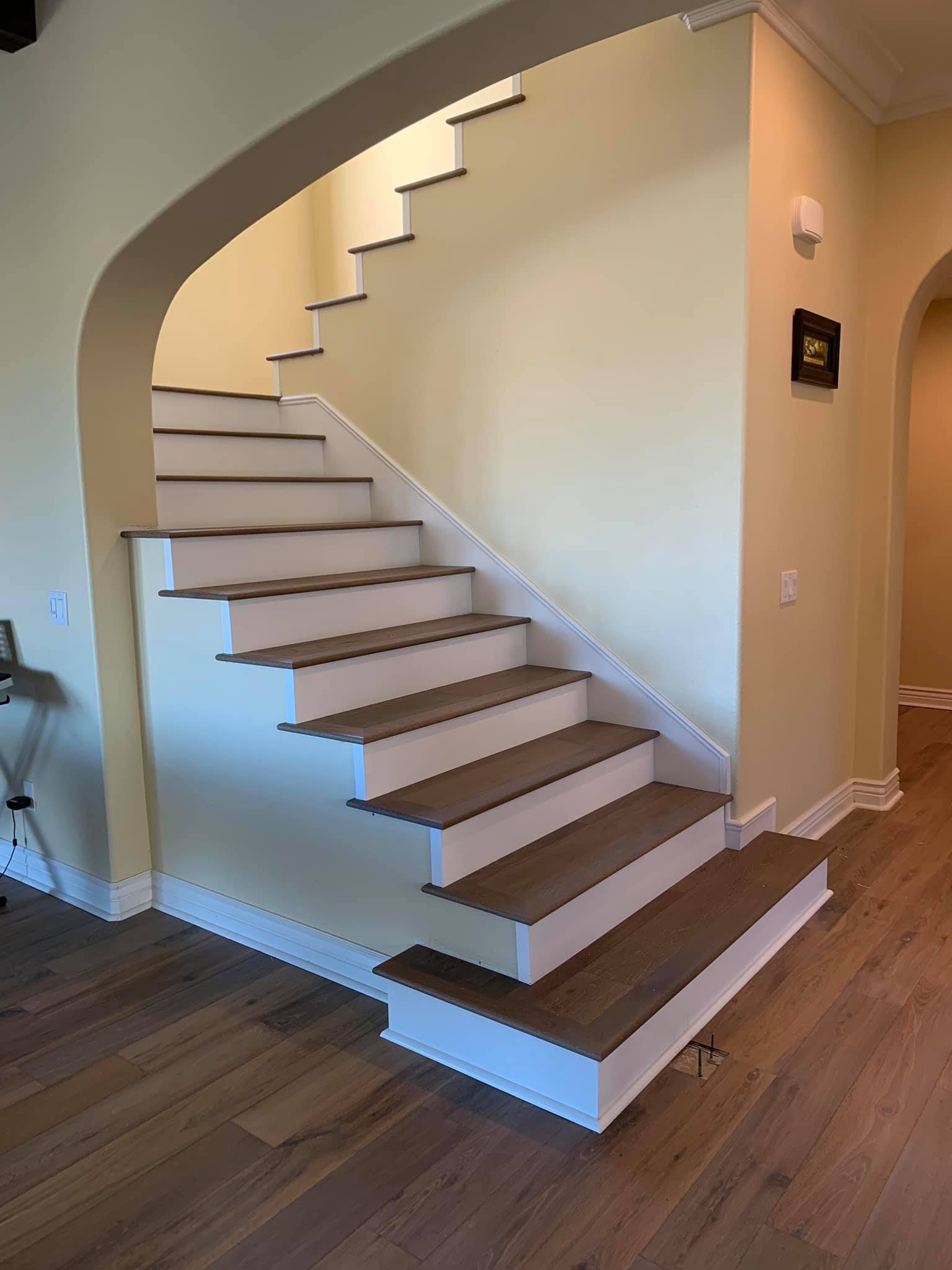 Photo of a staircase with wooden steps and white risers in a home interior, with yellow walls and hardwood flooring.