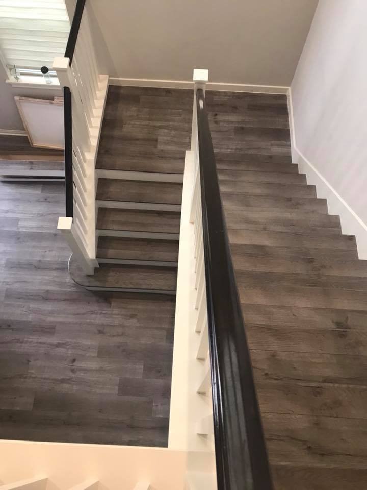 Top view of a staircase with dark wooden flooring, white railings, and a black handrail, seen from an upstairs landing.