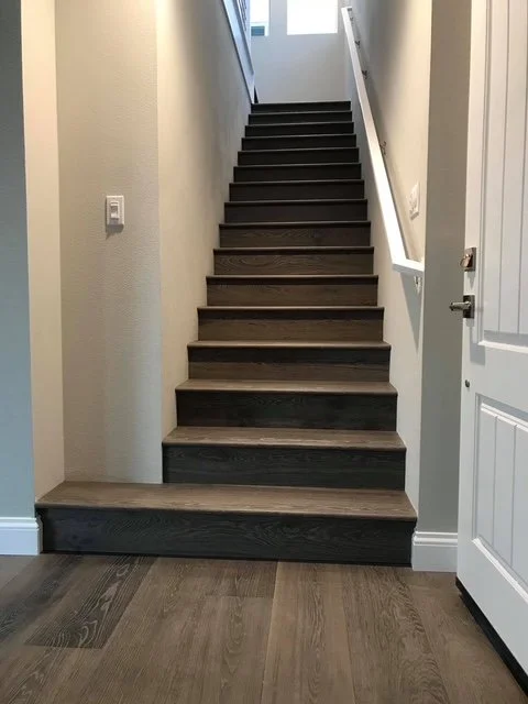 Interior view of a staircase with dark wood steps leading up to a bright window, located beside a white door and wall.