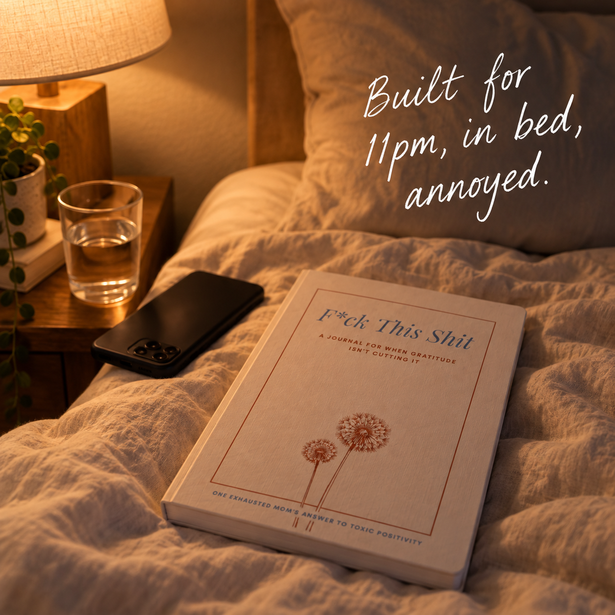 The Anti-Gratitude Journal on a rumpled bed beside a nightstand, lamp on
