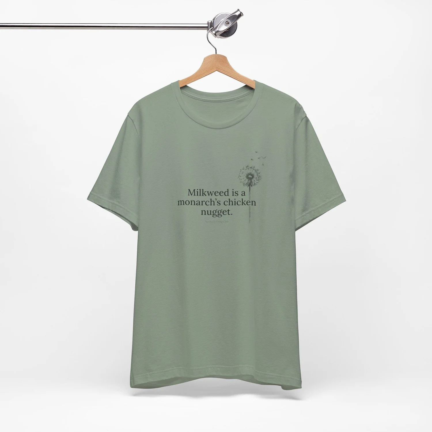 Heather Sage tee on a wooden hanger, printed in black with "Milkweed is a monarch's chicken nugget." and a dandelion going to seed