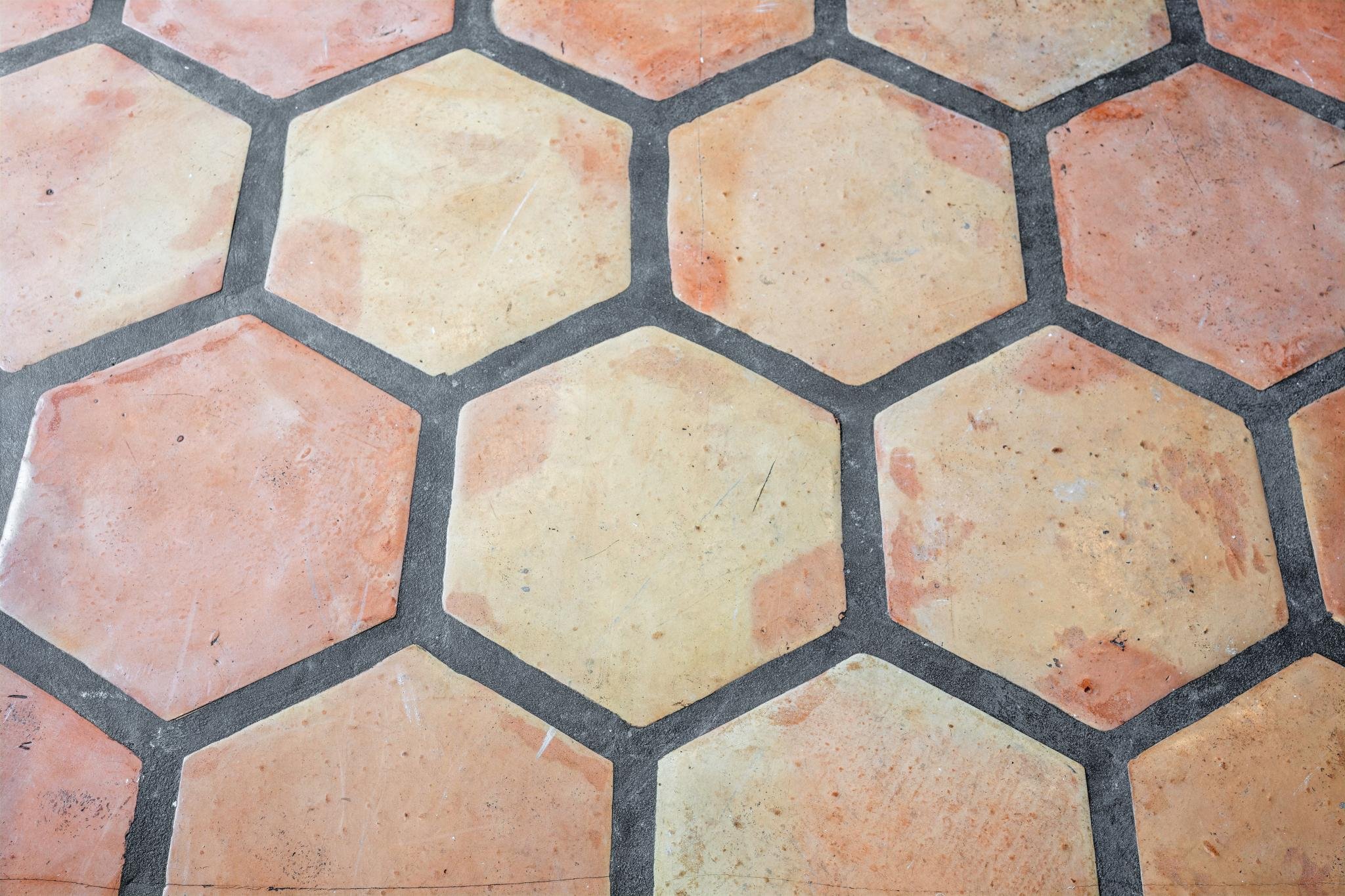 Close-up of a tiled floor with large, irregular-shaped, peach and beige tiles separated by dark gray grout lines.