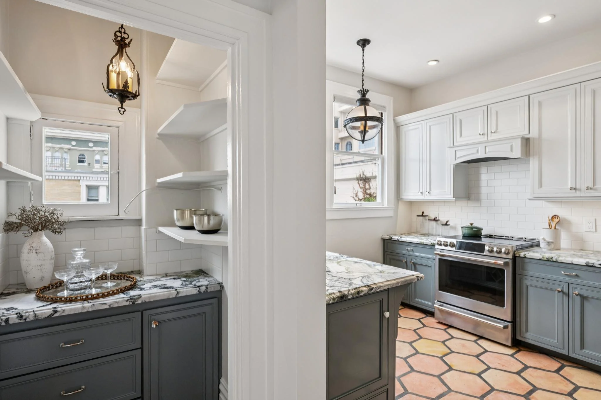 A kitchen with white cabinets, a marble countertop, and a window. There is a hanging light fixture and some decorative items on the counter.