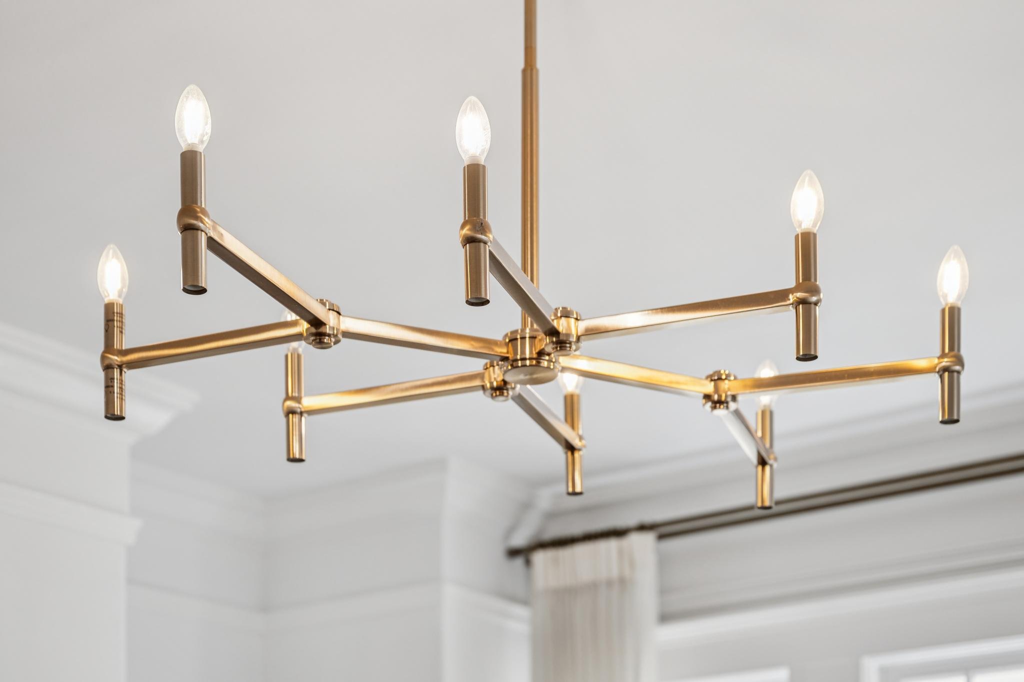 Close-up of a modern gold chandelier with multiple light bulbs against a white ceiling.