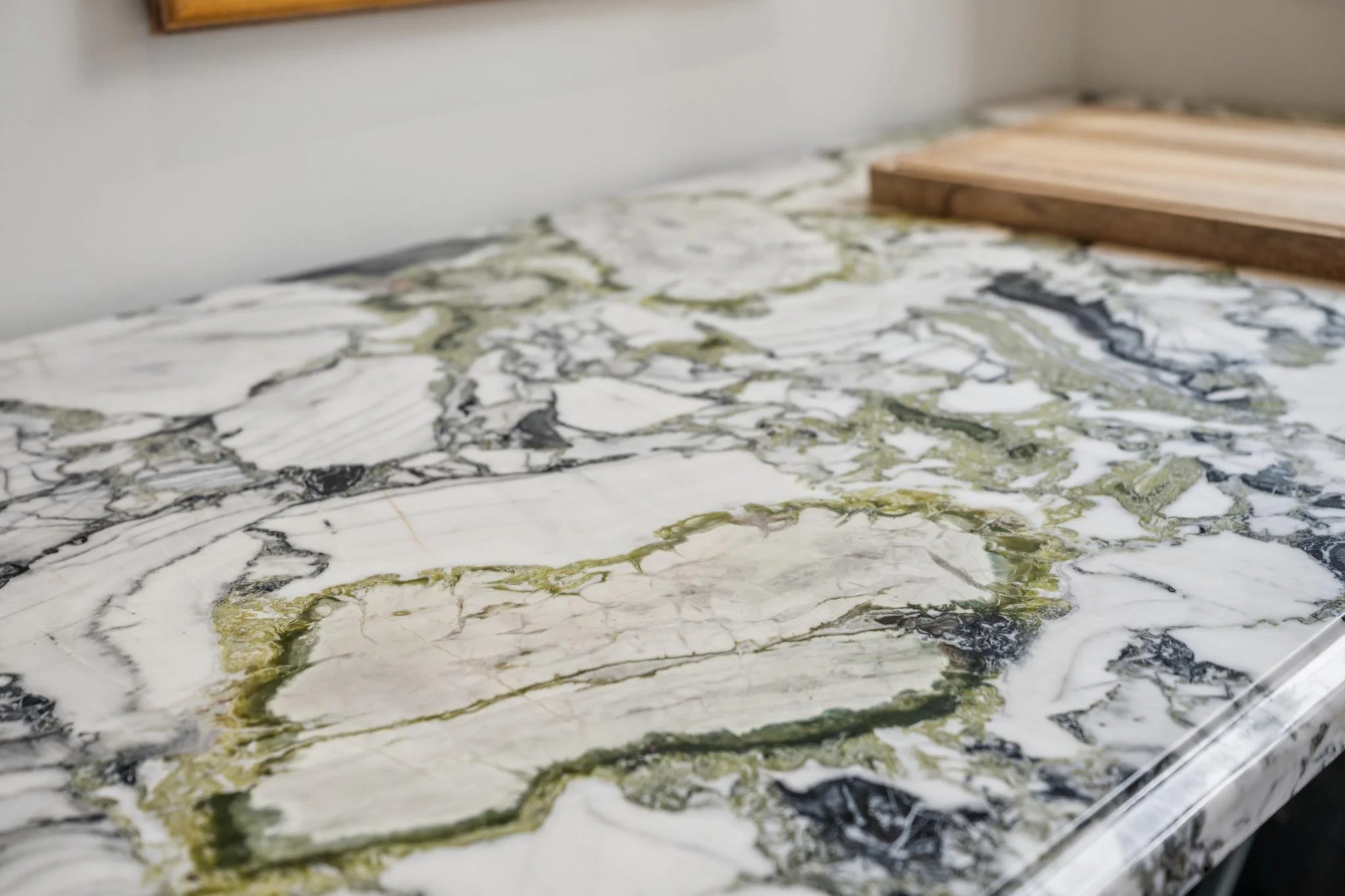 Close-up image of a marble countertop with black, white, and green veining, and a wooden cutting board on the edge.