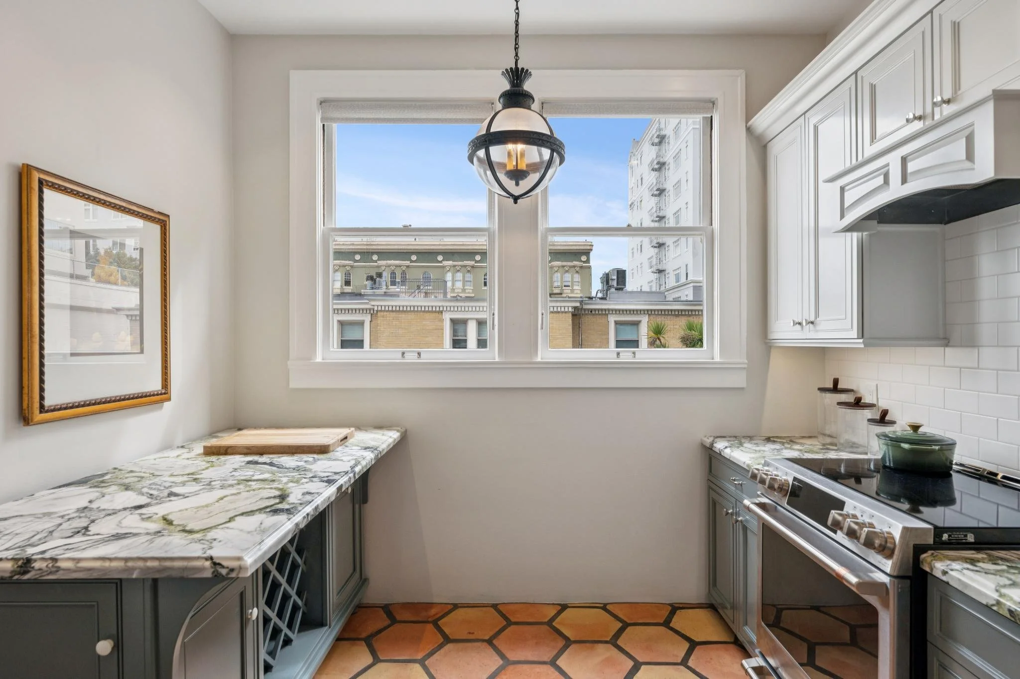 Kitchen with white cabinets, marble countertops, a stove, and a large window showing city buildings outside.