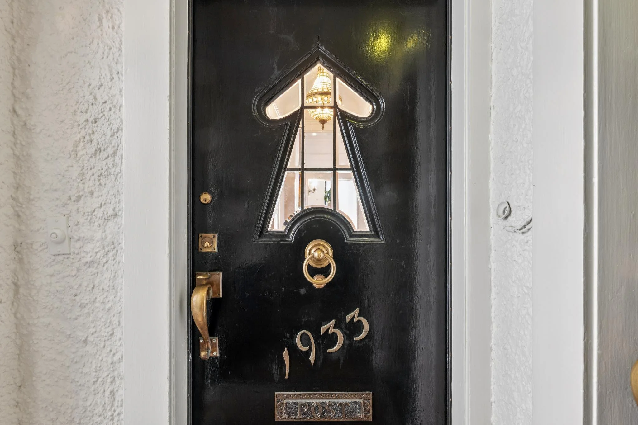 Close-up of a black front door with a heart-shaped cutout window, featuring glass panes, with a view of a chandelier inside the house.