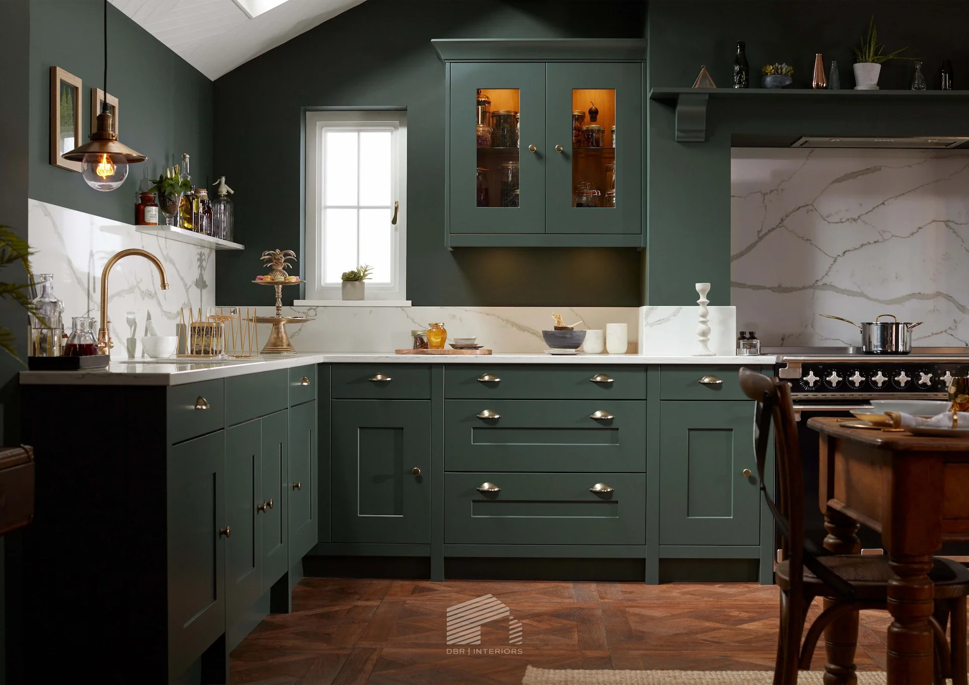 A kitchen with dark green cabinets, marble backsplash, and wooden flooring, featuring a window, hanging light, and various decorative items.