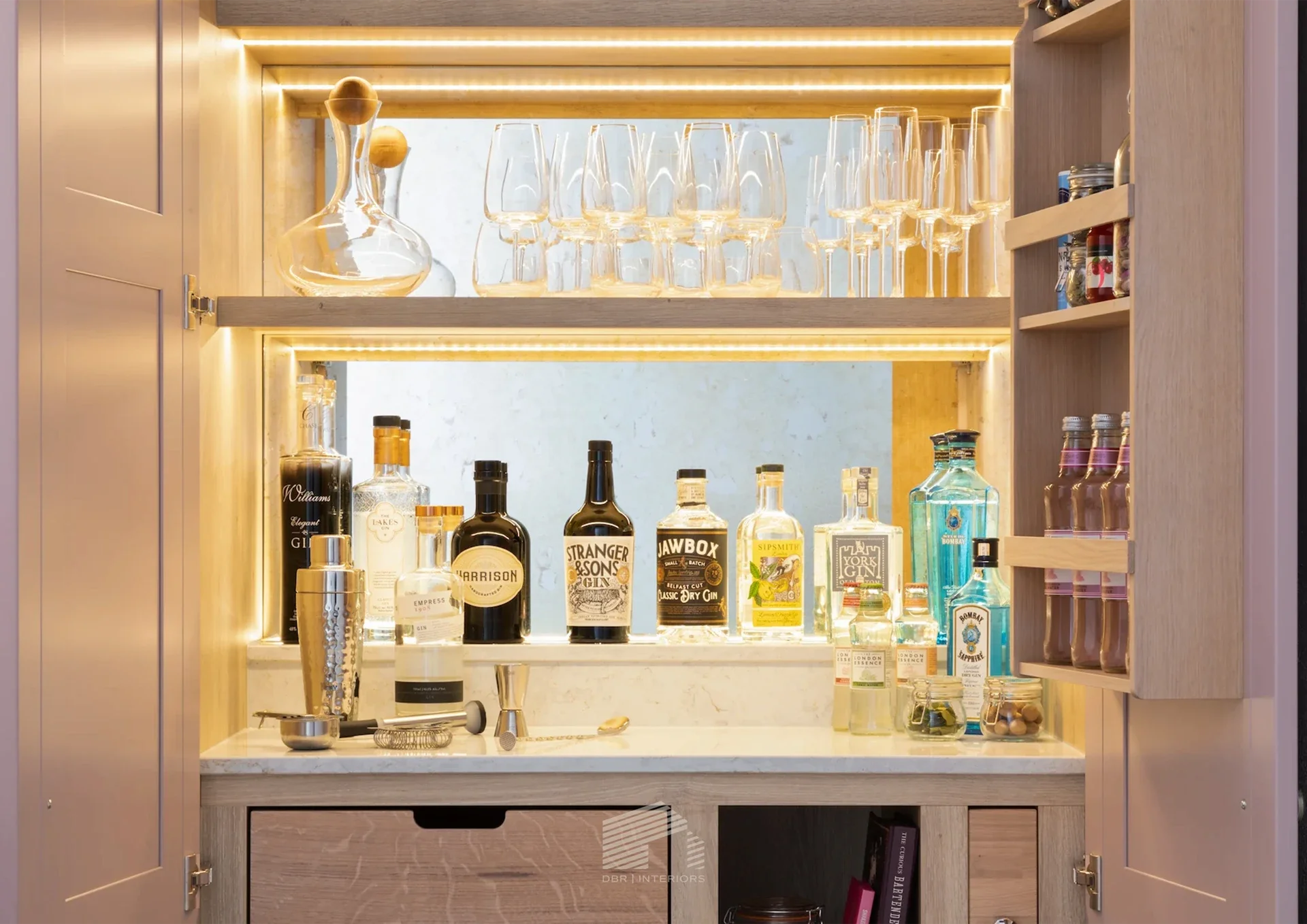 A wooden home bar cabinet with bottles of alcohol, glasses, and a decanter, featuring integrated lighting and wine storage on top.