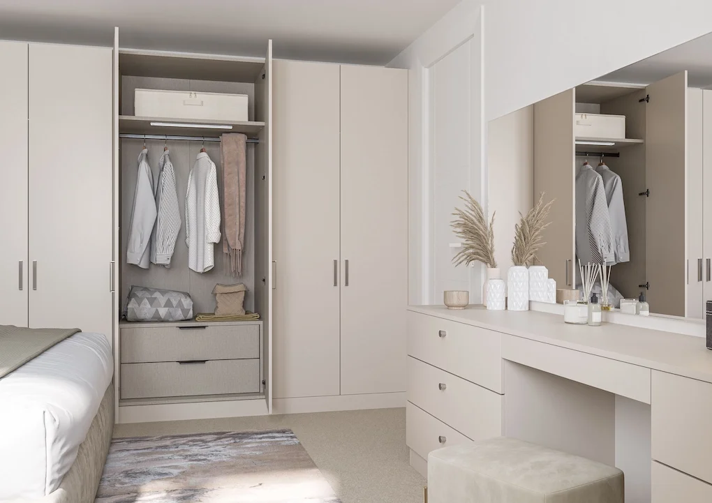 A minimalist bedroom with built-in white closets, a bed partially visible on the left, a dresser with decorative vases and dried plants in the center, and a large mirror on the right.