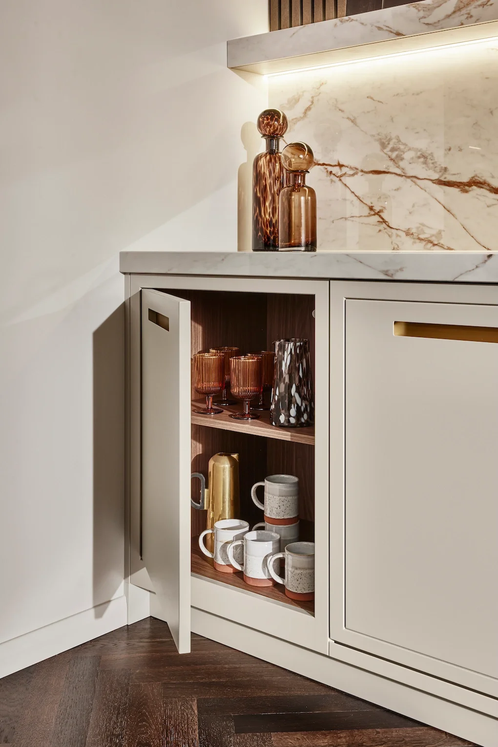 A white cabinet with a marble countertop and backsplash, decorated with amber glass vases and cups on the shelf, set in a modern kitchen or living space.
