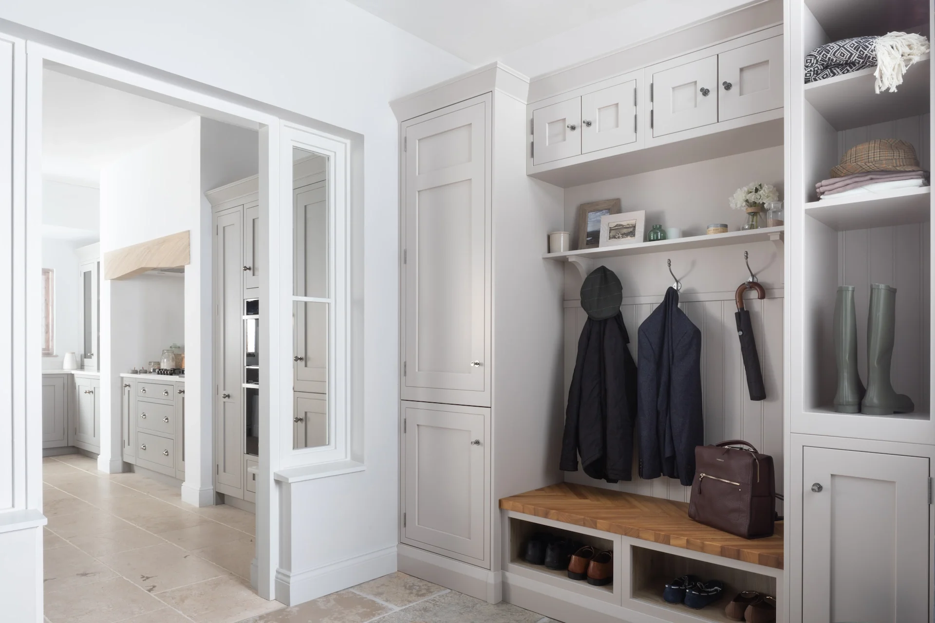 White cabinetry and a built-in bench with coat hooks in an entryway, with shoes and handbags on the bench and open shelving, in a home interior.