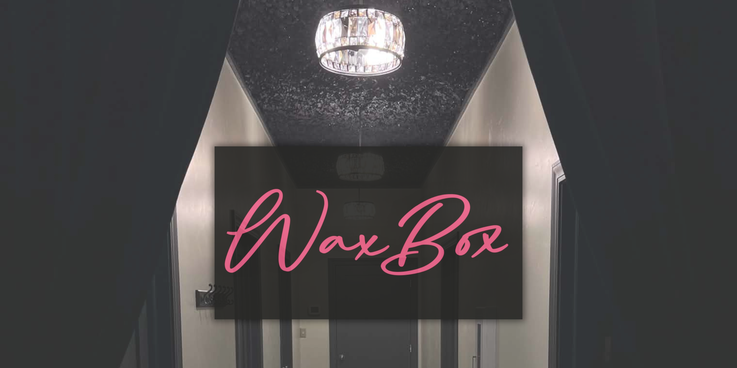 A hallway with dark walls and a black ceiling, featuring a modern chandelier and a sign that says 'Wax Box' in pink cursive font.
