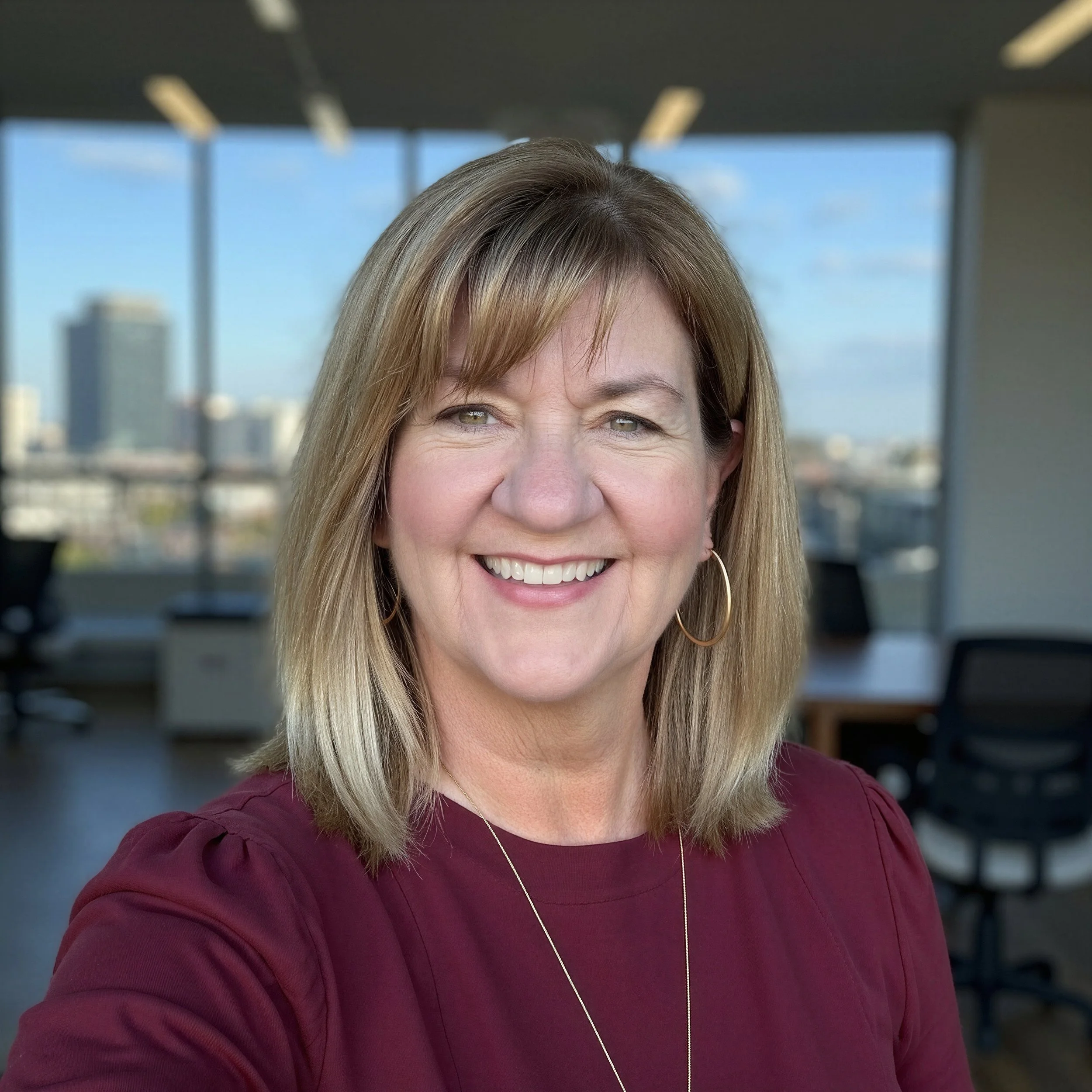 A close up headshot of Trinity Palms Ministries prayer ministry director, Lisa Nirva. She is smiling and wearing a maroon top with a business office background.