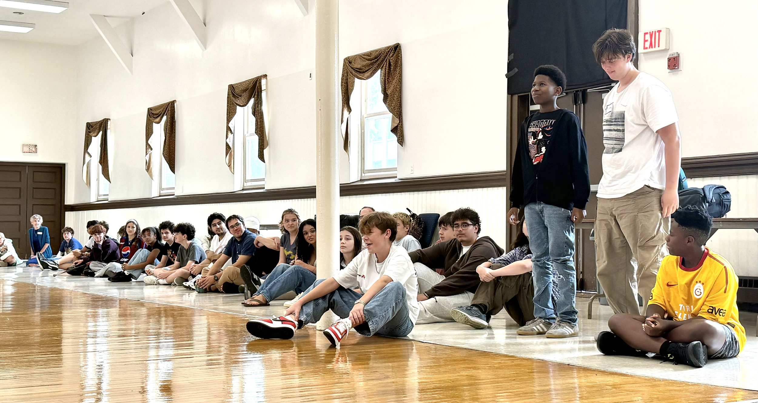 Students sitting in a circle, two students standing and speaking to the group.