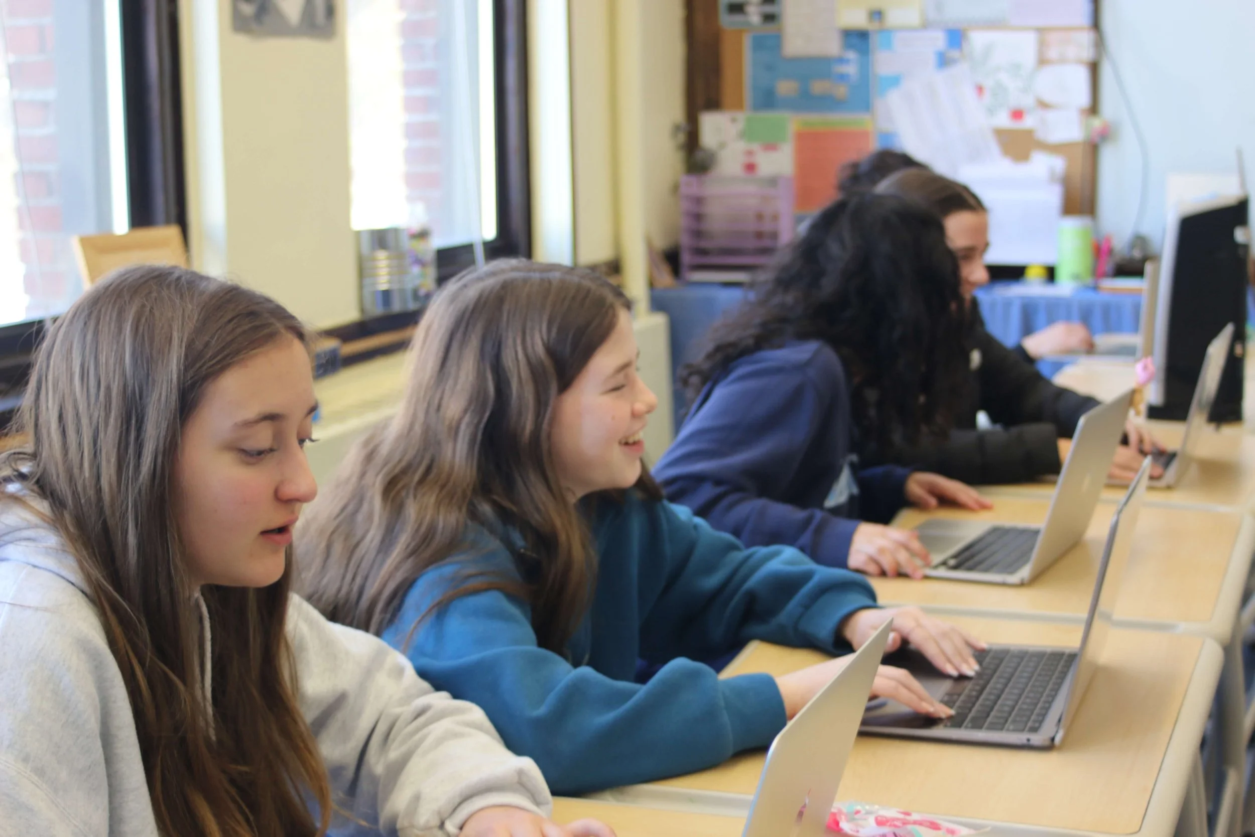 Four students working on laptops at a classroom desk.