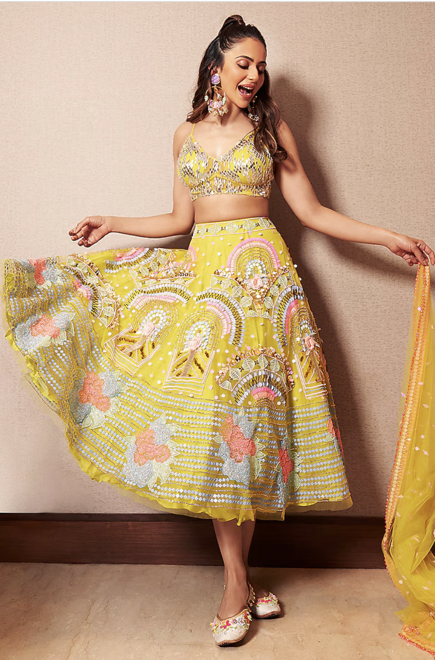 A woman dancing in a yellow embroidered skirt and matching crop top with floral jewelry.