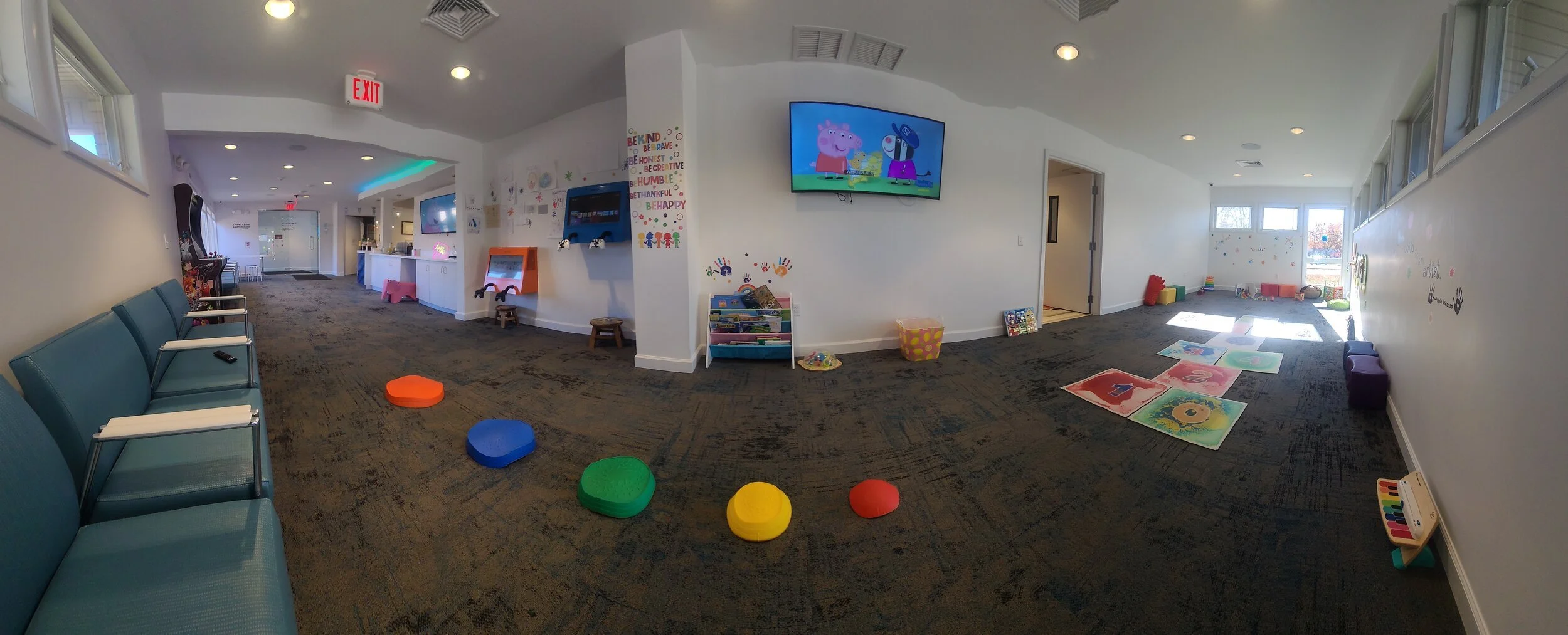 Children's playroom with seating, colorful toys, books, and large windows allowing sunlight.