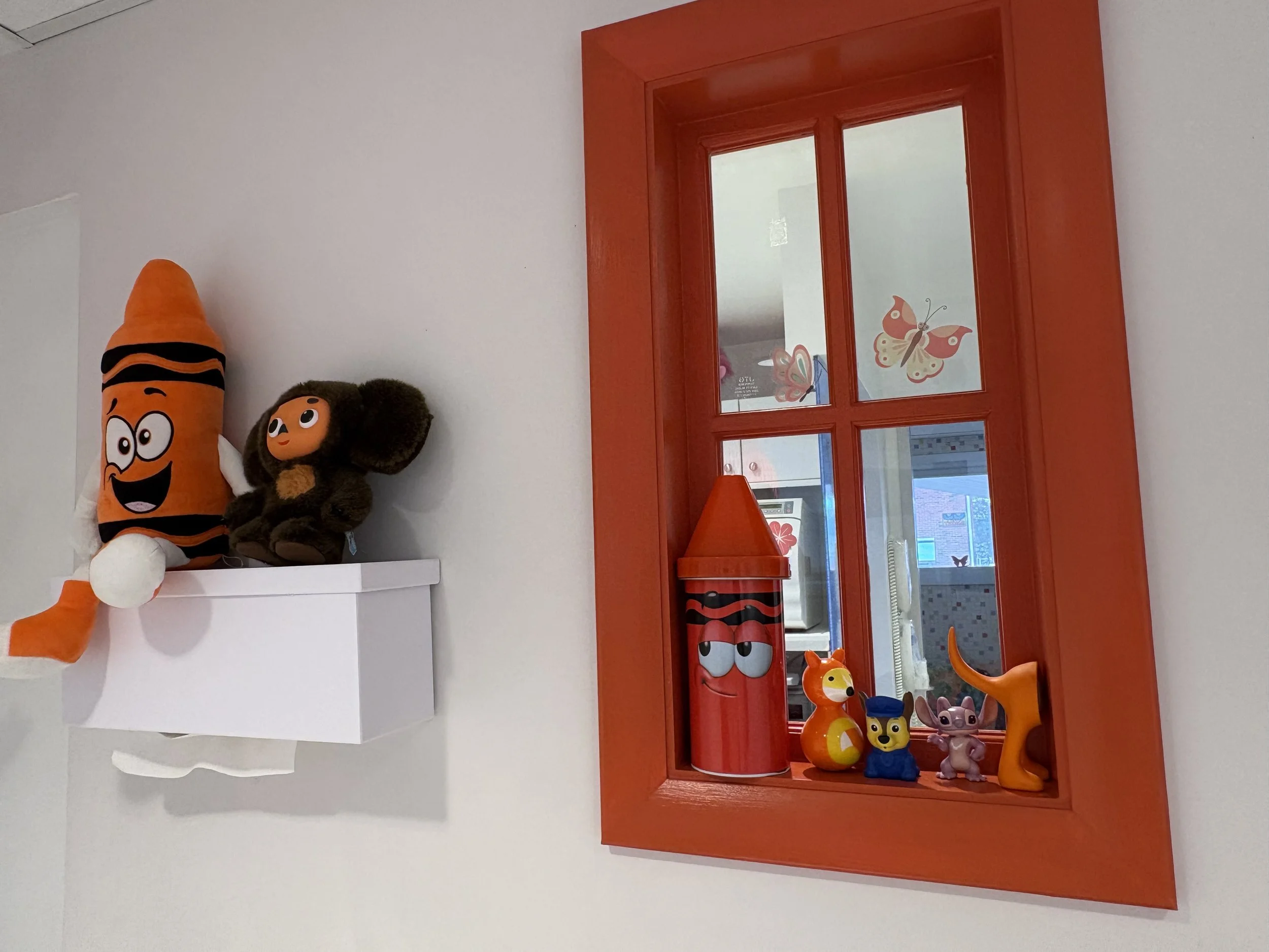 Colorful children's toy display with characters and figurines, reflected in a bright orange window, in a playful, vibrant setting.