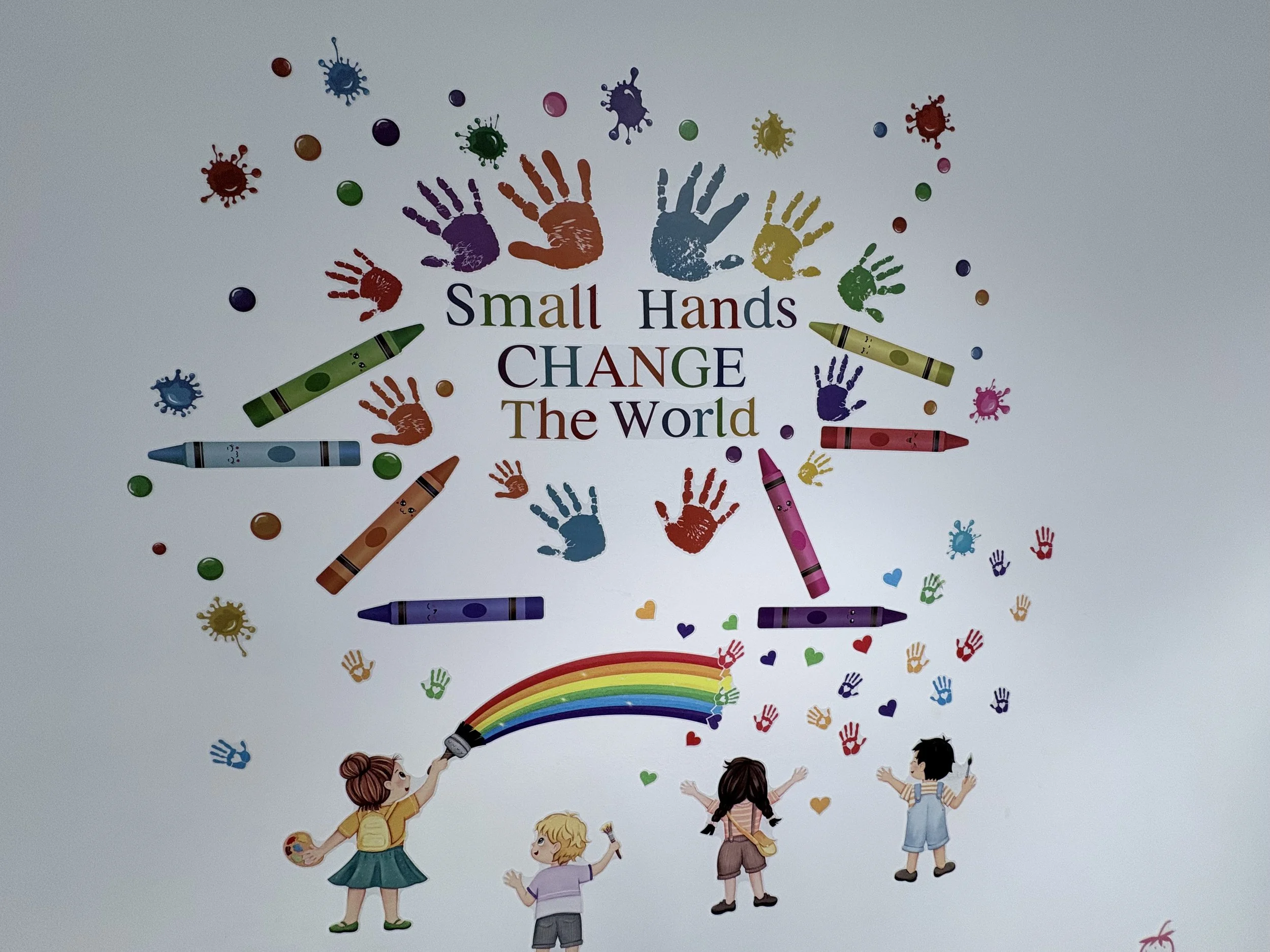 Colorful mural depicting children playing, holding crayons that create a rainbow, with handprints, crabs, and a rainbow at the top and bottom.
