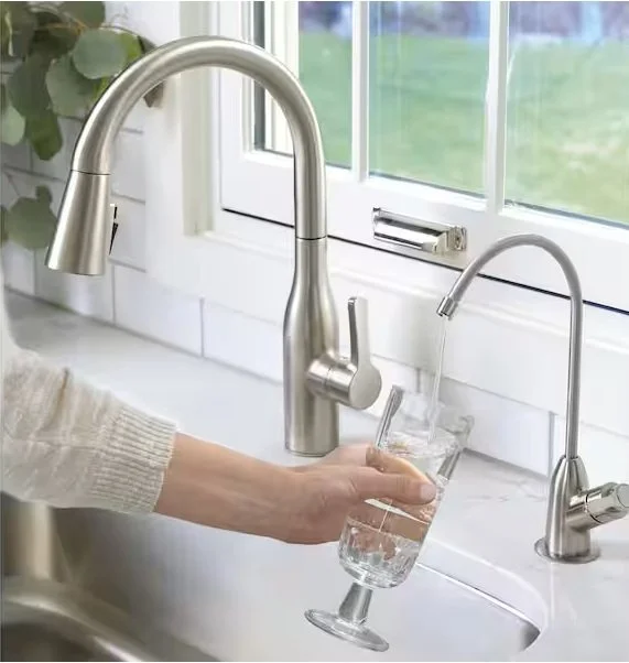 Person filling a glass with water from a kitchen sink faucet.