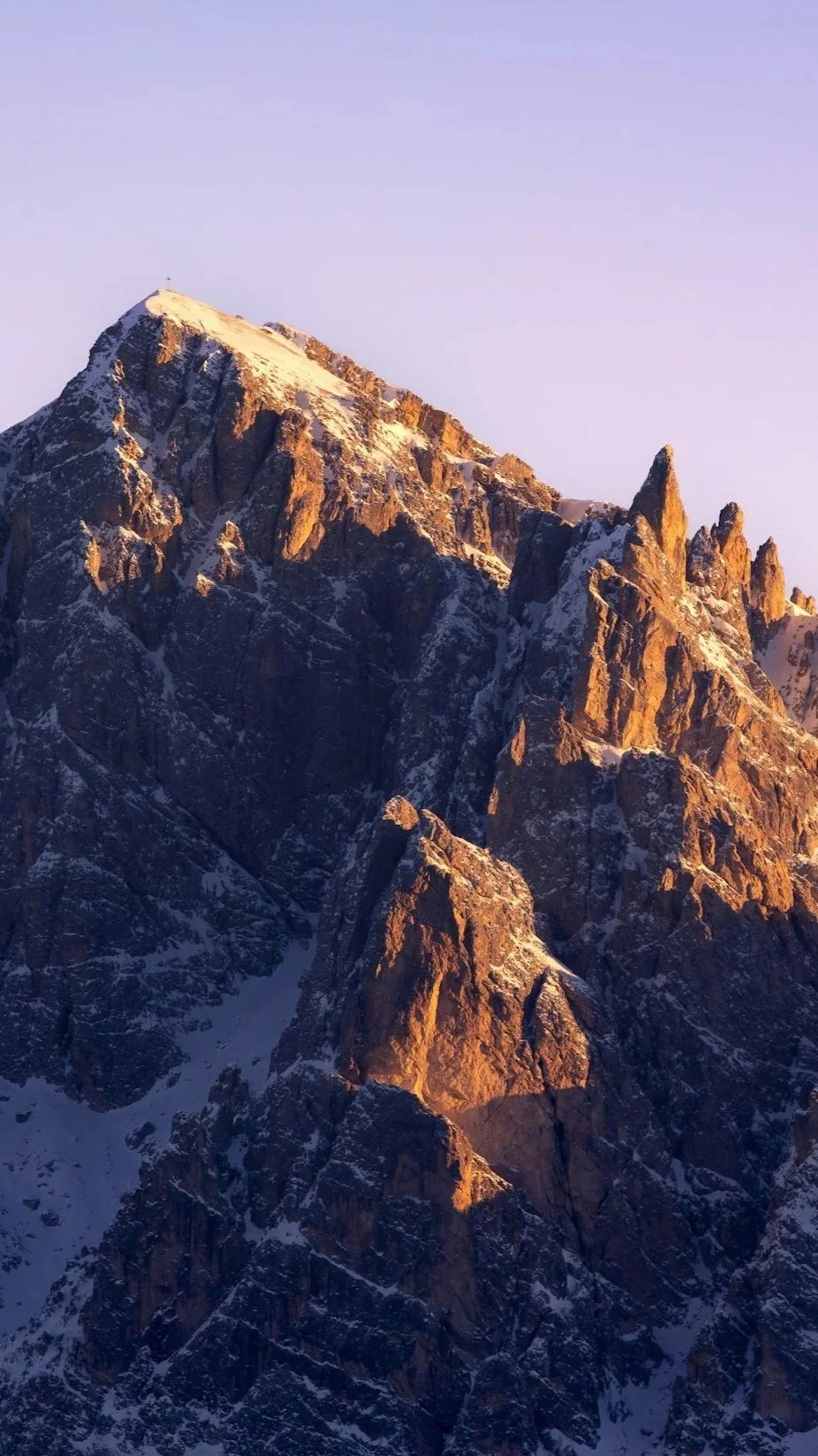 Snow-capped mountain peaks during sunset with rocky, rugged terrain.