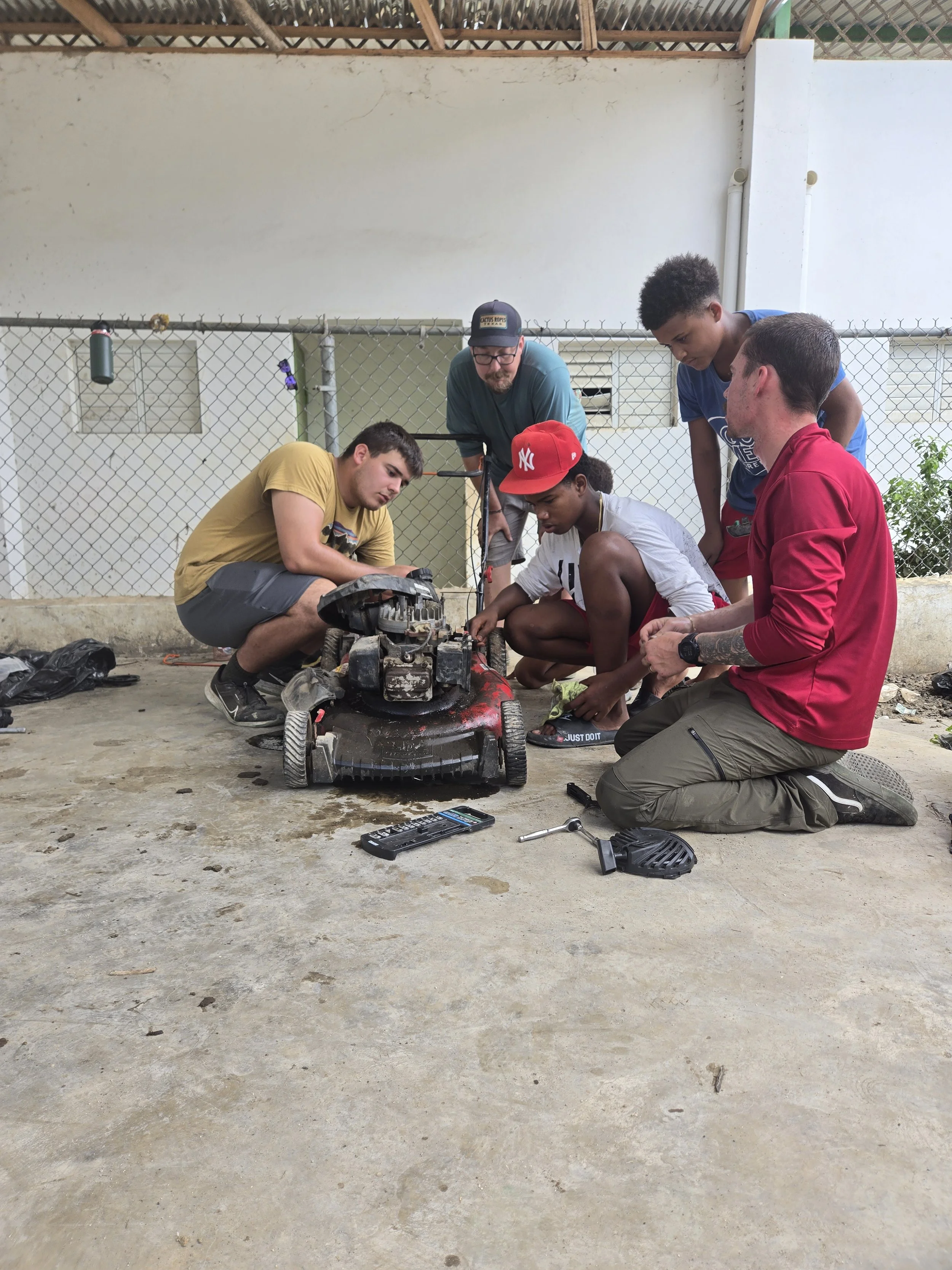 The Assurance team teaching young men how to repair their lawn mower in Dominican Republic.