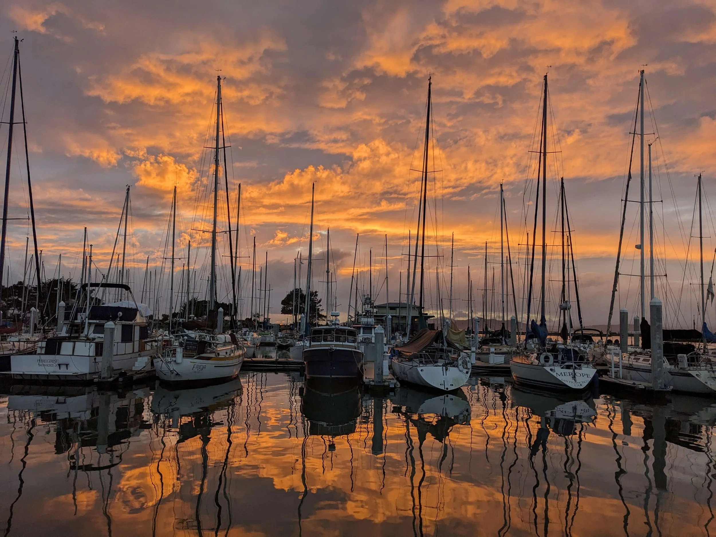 Marina with boats docked at sunset, reflecting orange and purple clouds in the water.