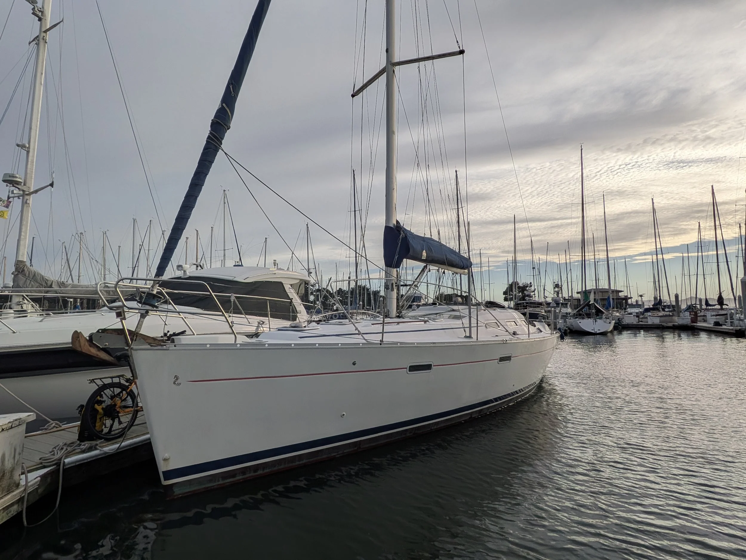 Several sailboats docked at a marina on a cloudy day, with the water reflecting the boats and sky.