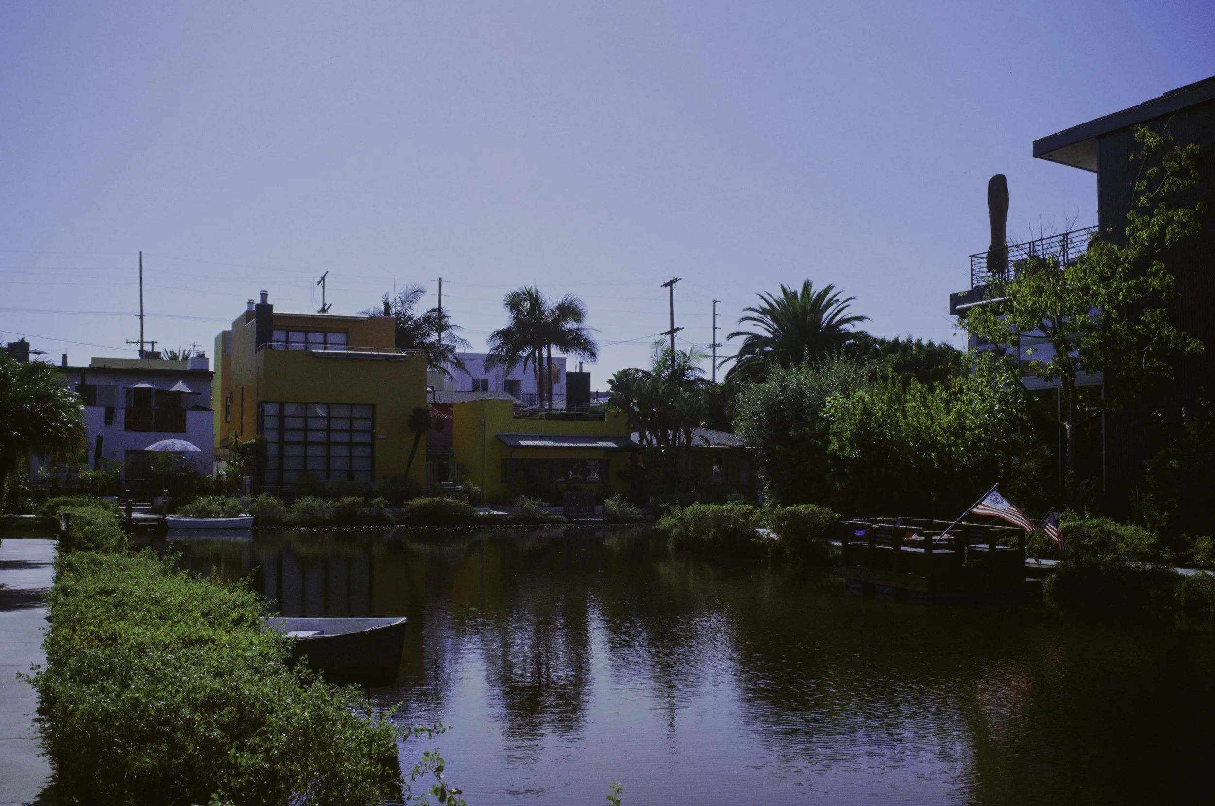 Residential neighborhood with colorful houses by a body of water, palm trees, and a blue sky.
