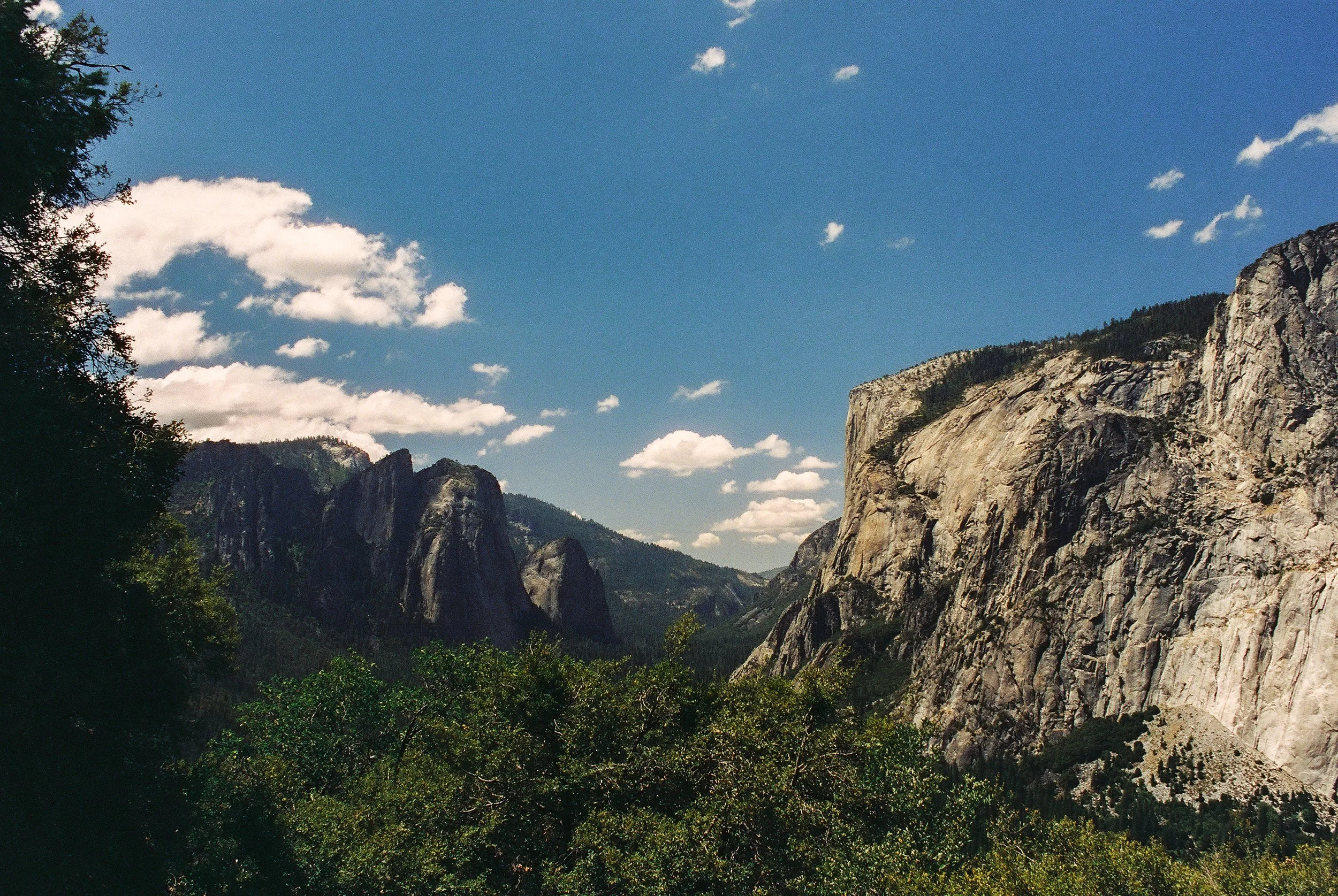 Scenic view of a mountain valley with steep cliffs, green trees, and a partly cloudy sky.