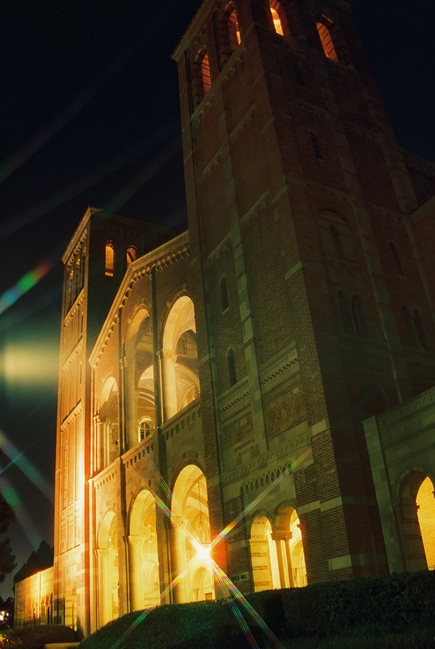 Night view of a historic brick building with illuminated arches and windows, with a bright light shining in front, creating lens flares.